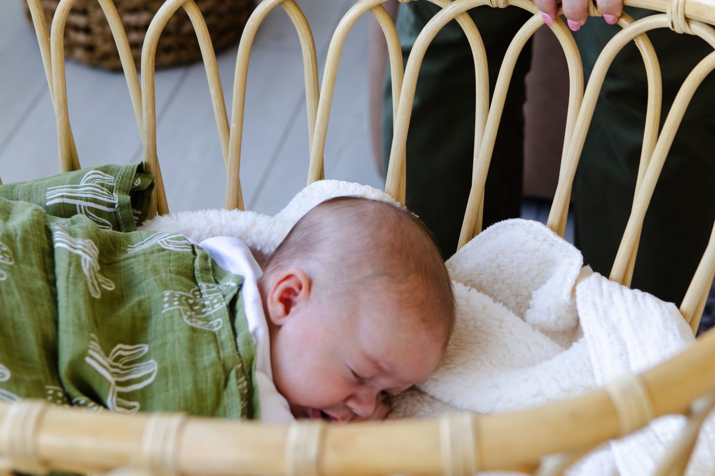 Newborn baby wrapped in a green blanket with white patterns, lying in a wicker basket.