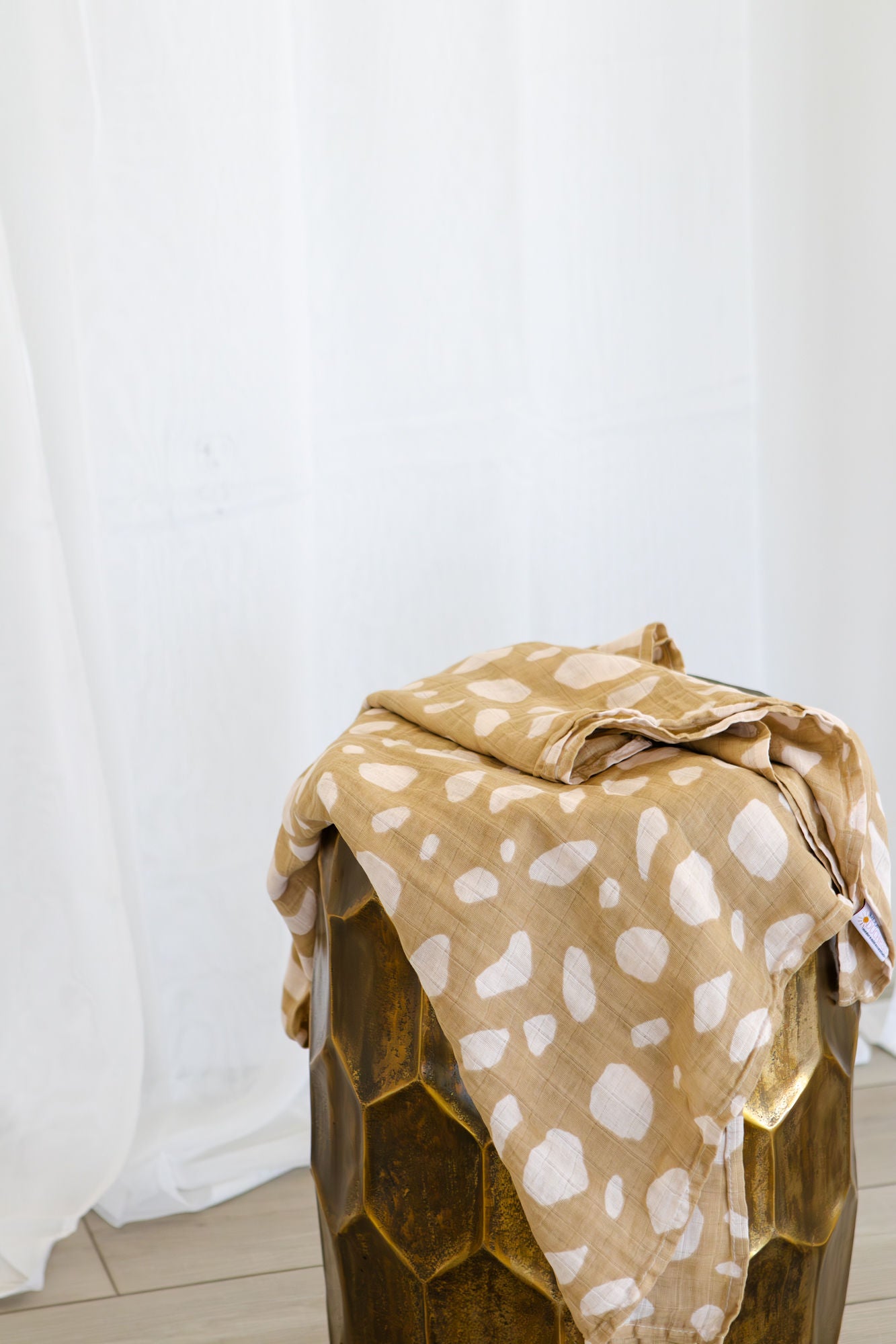Beige blanket with white patterns draped over a wooden stool against a white curtain background