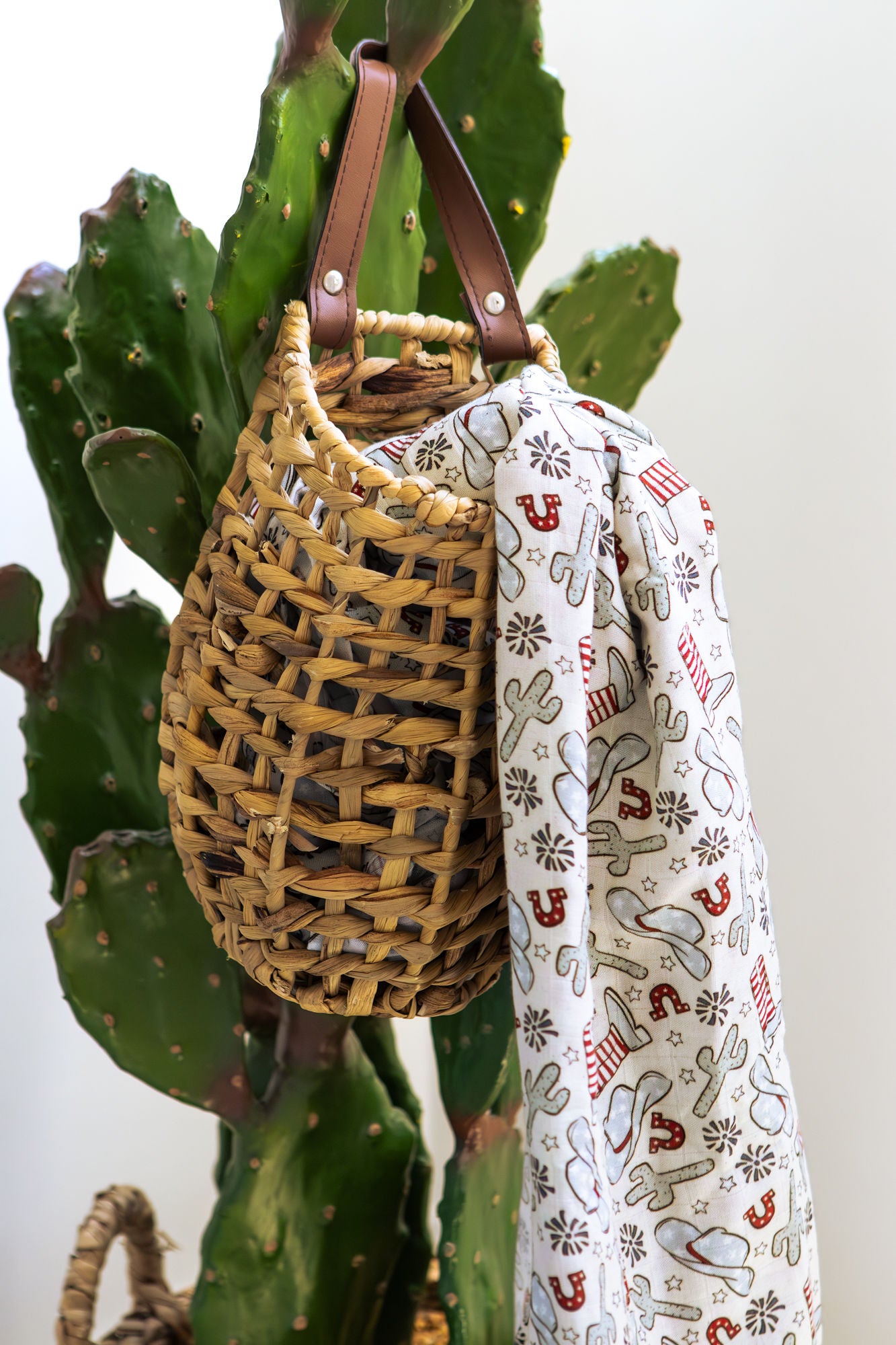 Woven bag with a strap draped over a plant and a patterned fabric with Christmas designs.