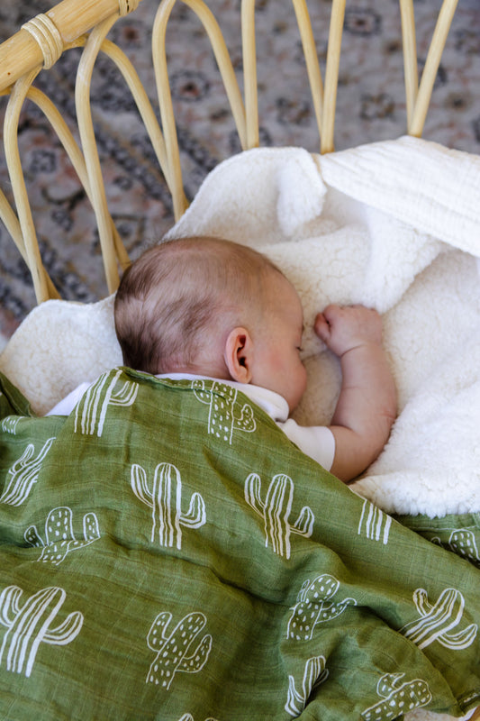 Baby sleeping under a green blanket with cactus patterns on a textured surface