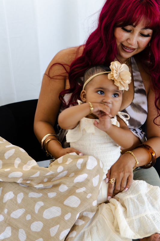 Woman with red hair holding a baby wearing a white dress with a beige flower headband.