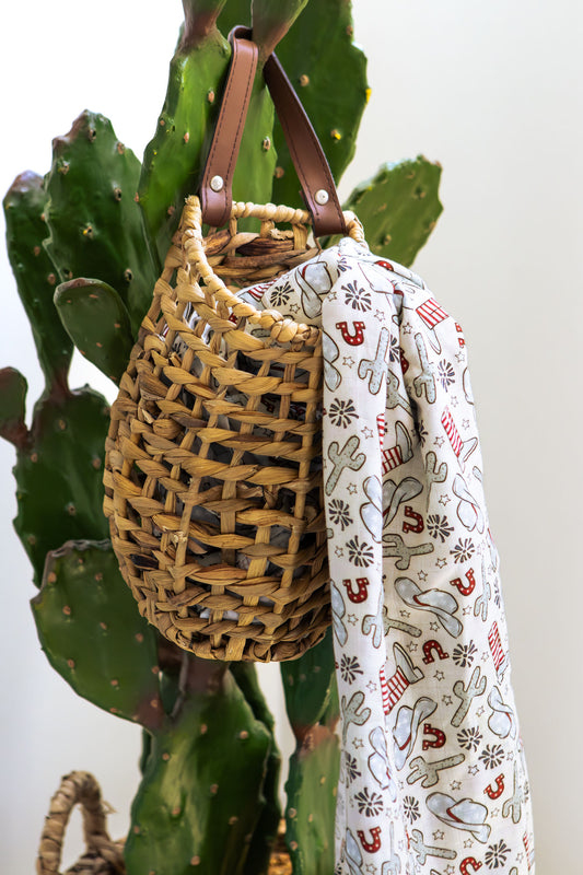Woven bag with a strap draped over a plant and a patterned fabric with Christmas designs.